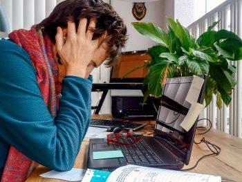 Foto van vrouw achter laptop. De vrouw heeft de handen in het haar. Ze komt er niet meer. Burnout of burn-out verschijnselen?